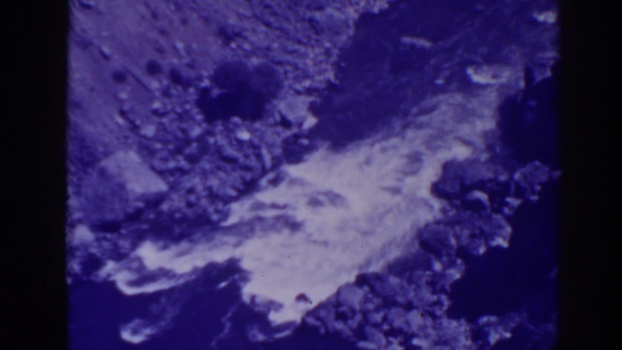 Rocky canyon terrain and a pale stream or road edge seen through purple-blue 8mm film.