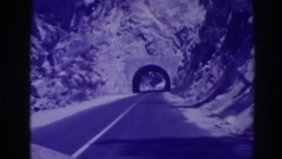 Late-frame view of the 1938 Oroville road approach, with the tunnel portal ahead and rock faces on both sides.