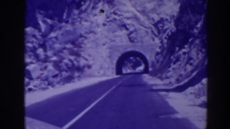 1938 Oroville, California home-movie frame showing a paved mountain road approaching a stone or rock tunnel entrance.