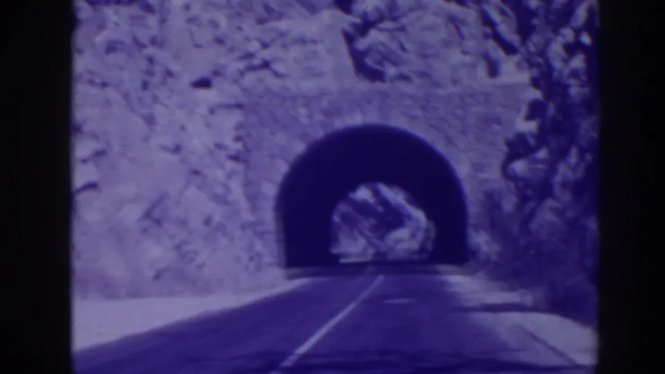 1938 home-movie frame with a closer view of the Oroville road tunnel, showing the dark arch and rocky roadside walls.