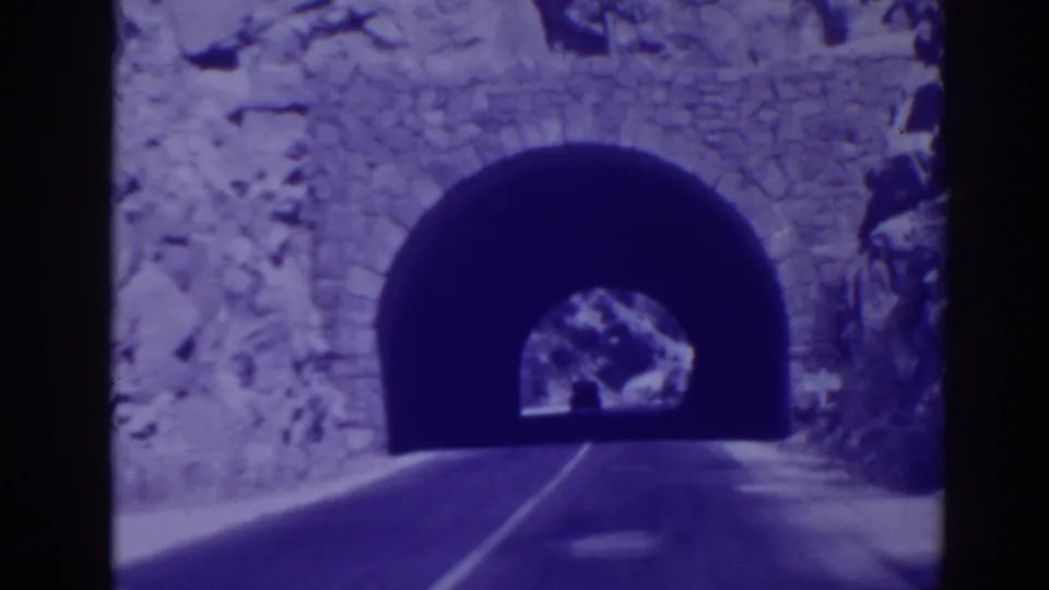 Close 8mm frame from Oroville showing the road entering a dark arched tunnel with rock and stone texture around the portal.