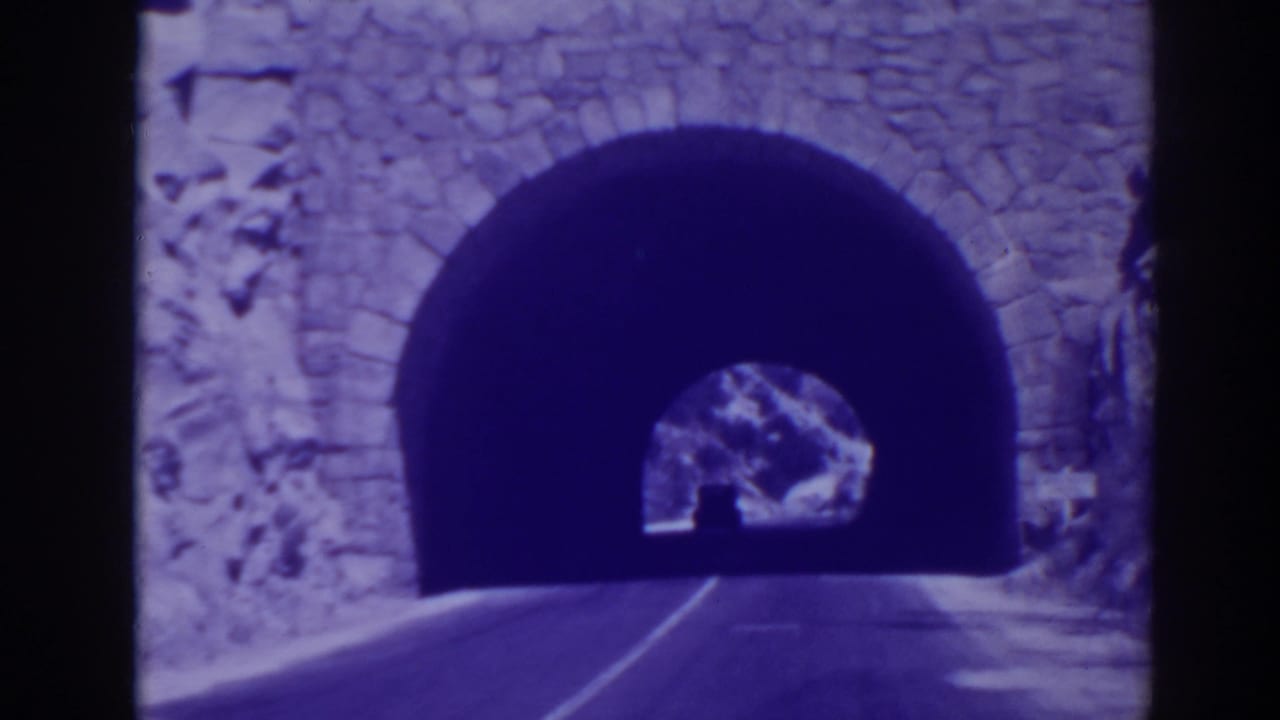 Paved road approaching a stone arch tunnel in a rocky hillside.