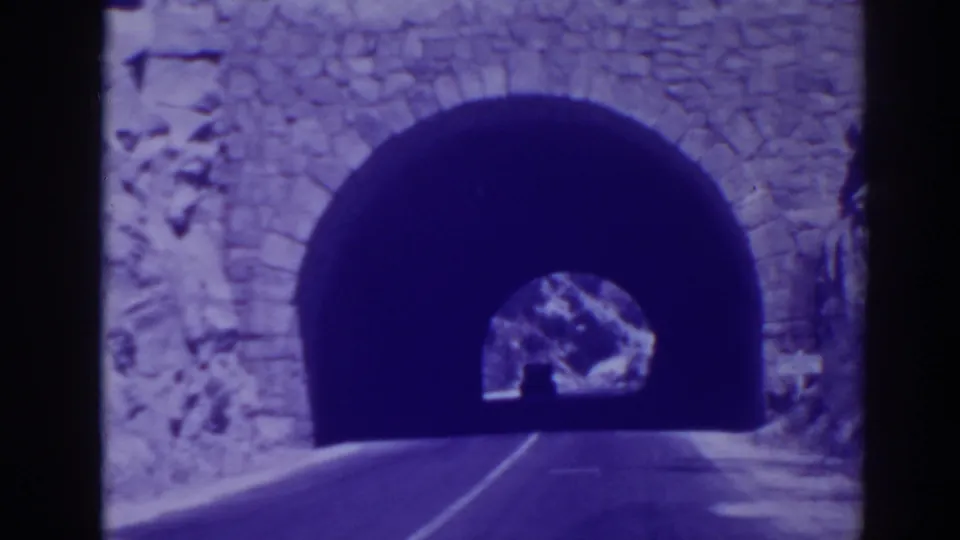 1938 Oroville footage shows a road leading toward a dark stone-arched tunnel opening set into rock.