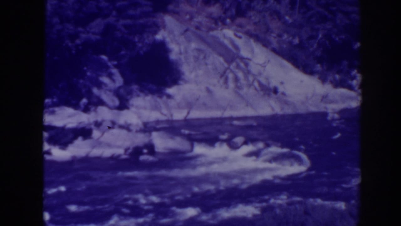1938 Oroville, California home-movie frame showing white water moving through rocks below a brushy hillside.