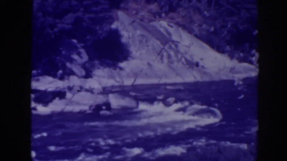 1938 Oroville, California home-movie frame showing white water moving through rocks below a brushy hillside.