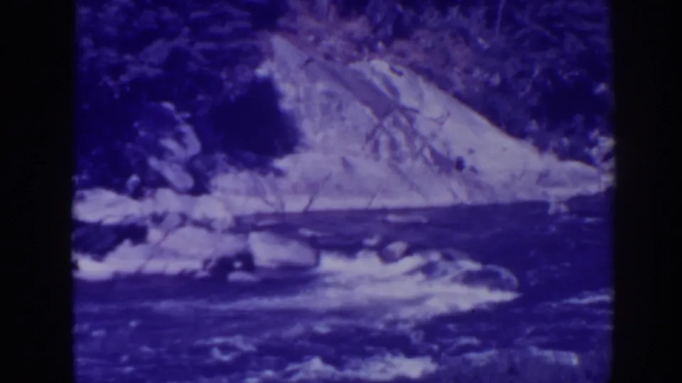 Late-1930s Oroville, California frame showing a rocky stream and wooded slope with strong blue-purple film color shift.