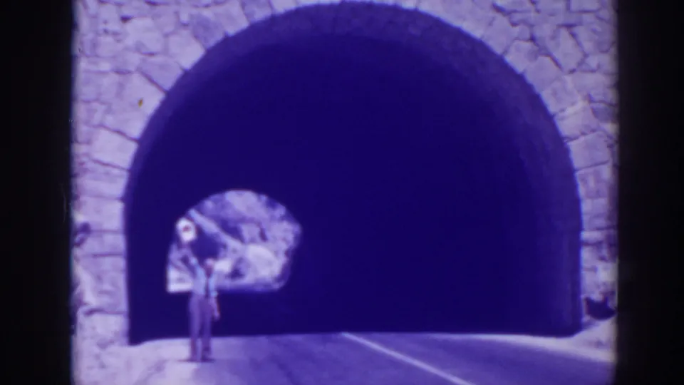 1938 Oroville frame showing a distant person standing by a large stone arch or tunnel opening beside a paved road.