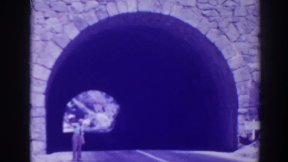 Blue-tinted Oroville footage shows a person near a stone arched opening, with roadway markings leading into the dark passage.