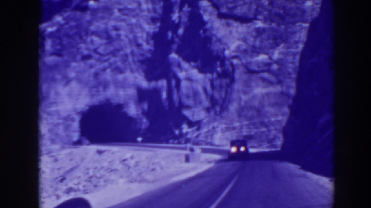 Car headlights approach a dark tunnel along a rocky mountain road.