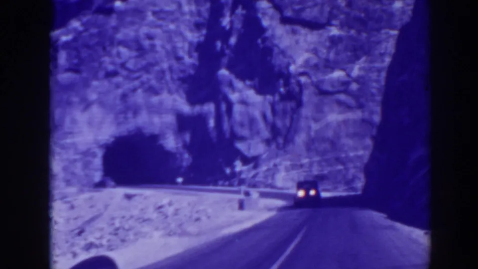 A vintage car approaches a dark tunnel opening on a winding road below a rugged rock face near Oroville, California.