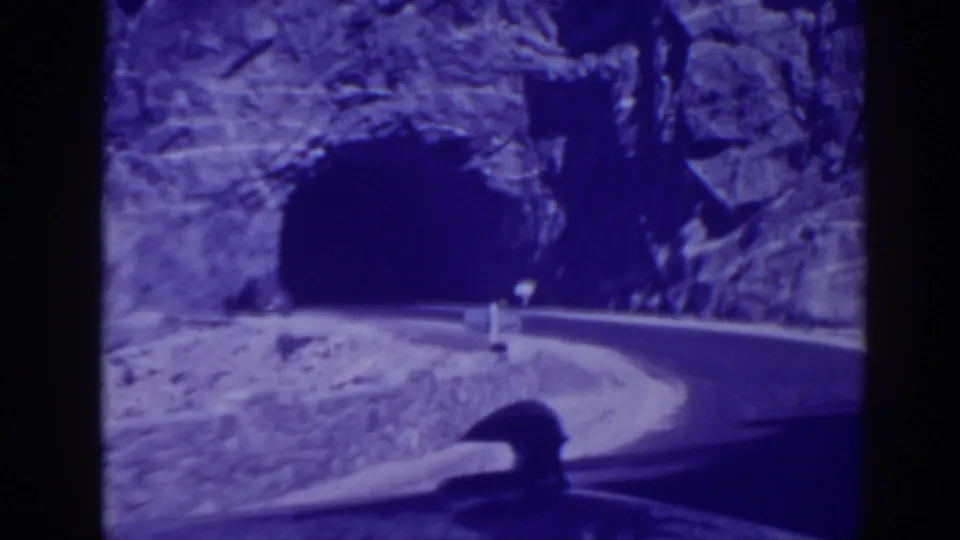 The road curves toward a dark tunnel cut into a rocky hillside, with the mountain route visible in the 1938 Oroville home movie.