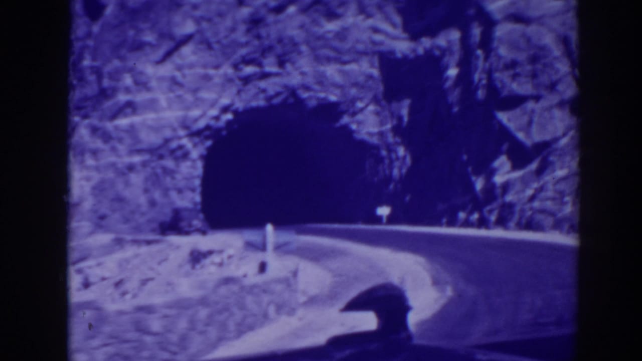 Curving mountain road leading toward a dark tunnel entrance with a car ahead.