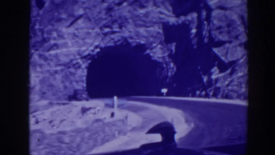 1938 Oroville road scene showing a car approaching a dark tunnel cut into a rocky hillside.