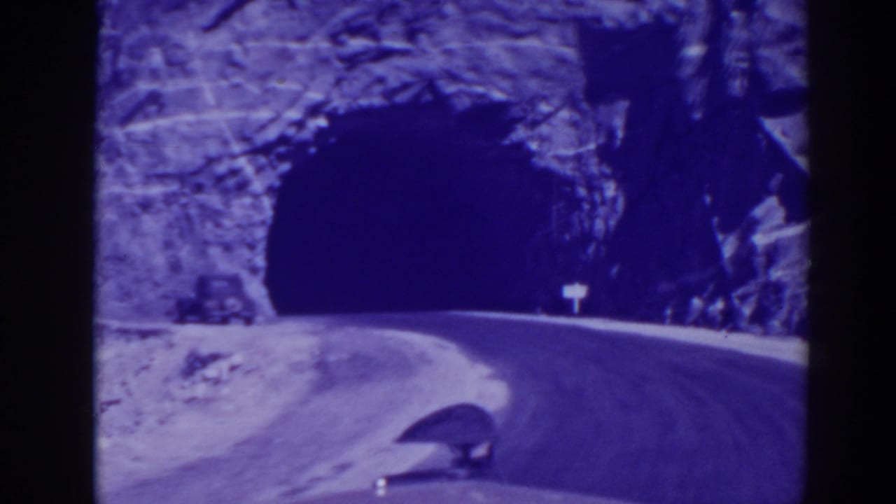 Automobile near a dark tunnel entrance on a curving road through rock.