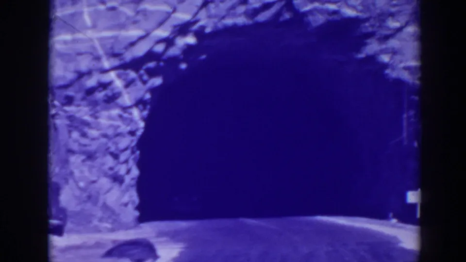 Close view of the tunnel mouth and roadway as the vehicle nears or enters the dark opening.
