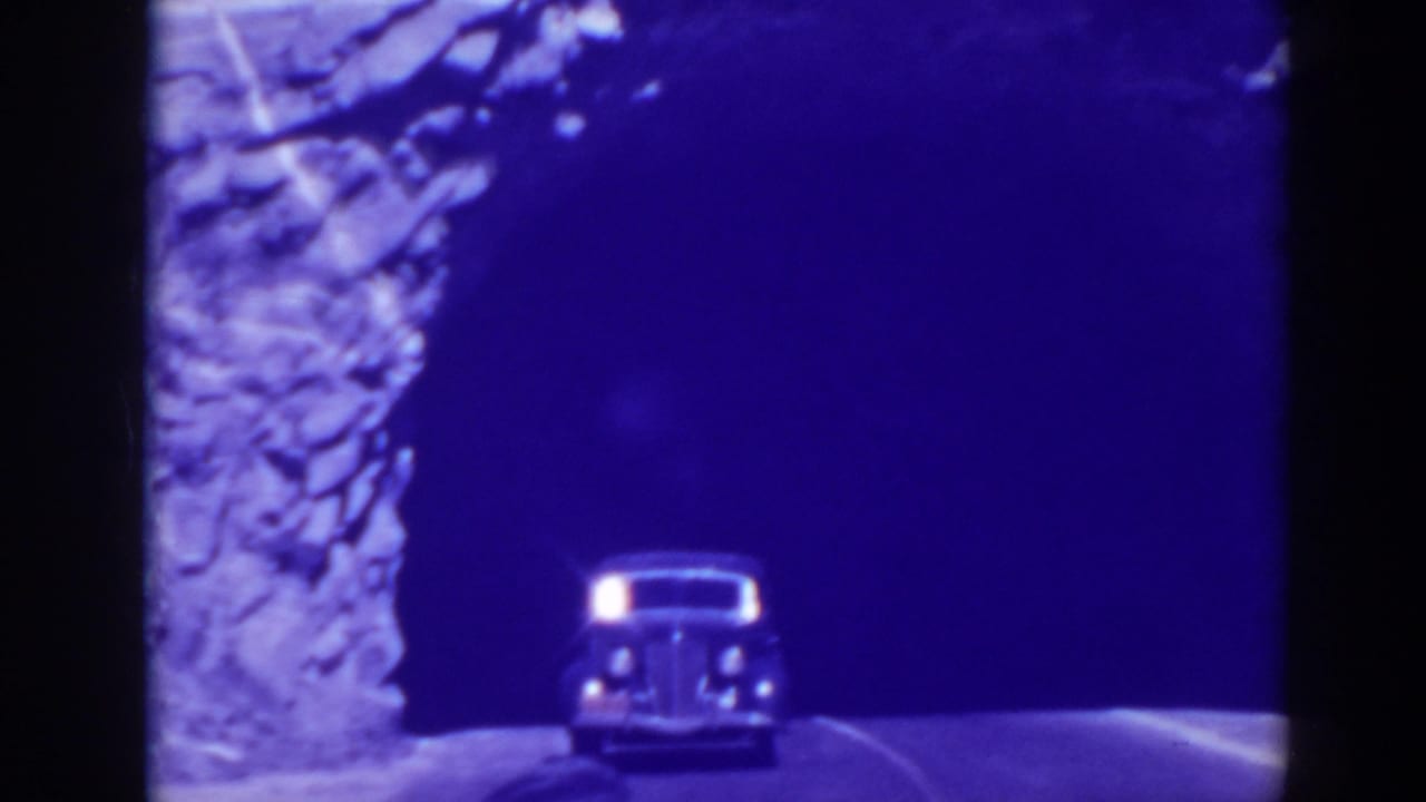 Vintage car emerging from a dark tunnel on a narrow road beside a rocky wall.