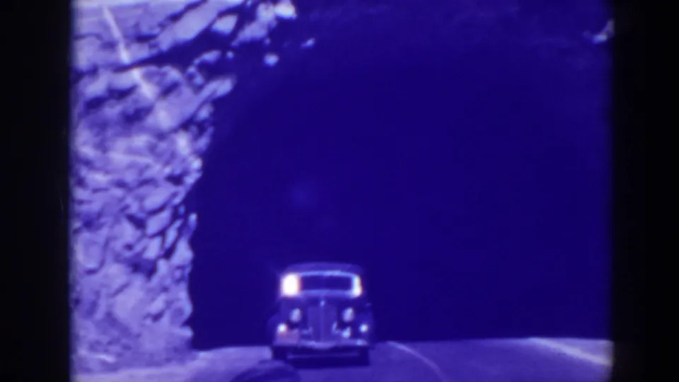 1938 Oroville home-movie frame showing a rounded car approaching from a dark tunnel beside a rock face.