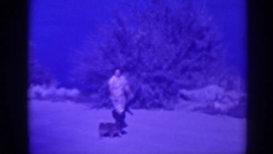 1938 Oroville home-movie frame of a woman walking a small dog along a dirt path near brush and rocks.