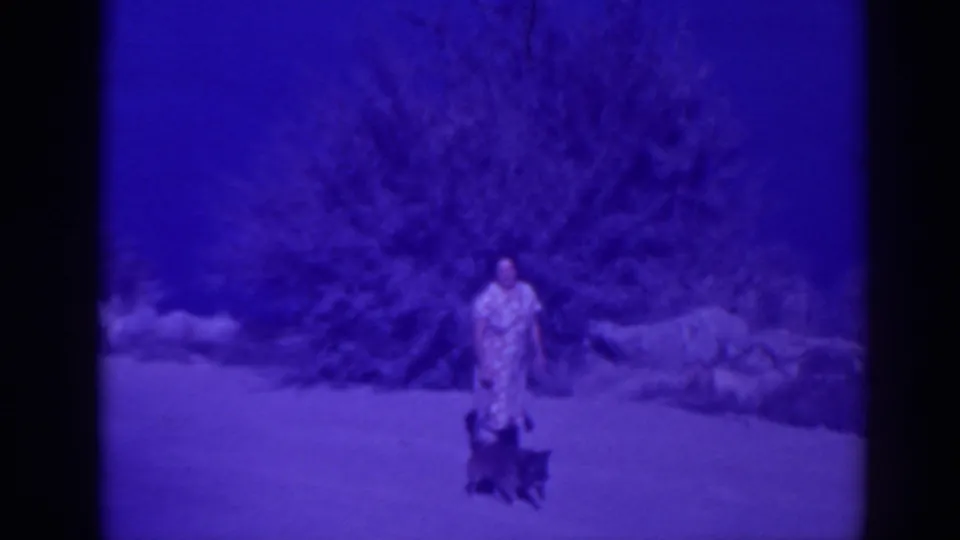 1938 Oroville frame showing a woman and small dog on open ground with shrubs and rocks behind them.