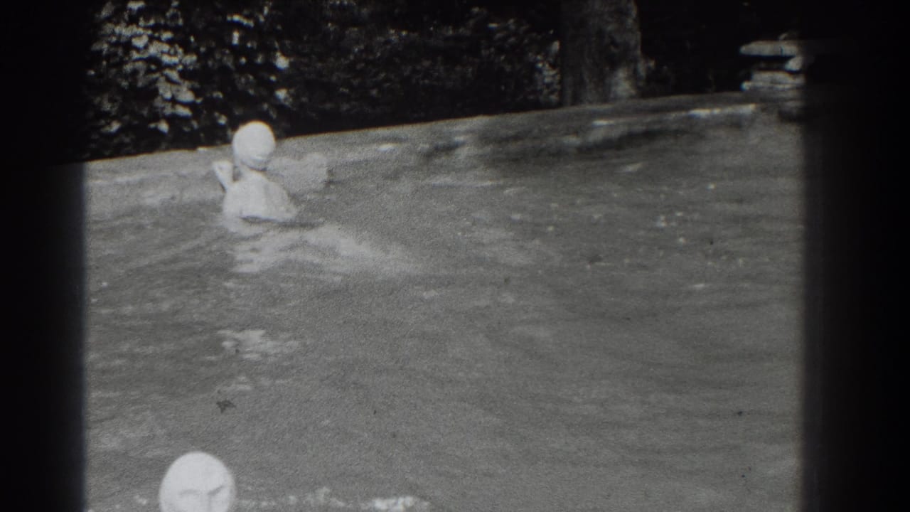 Two swim-capped people in an outdoor pool, with one near the foreground and one near the far edge.