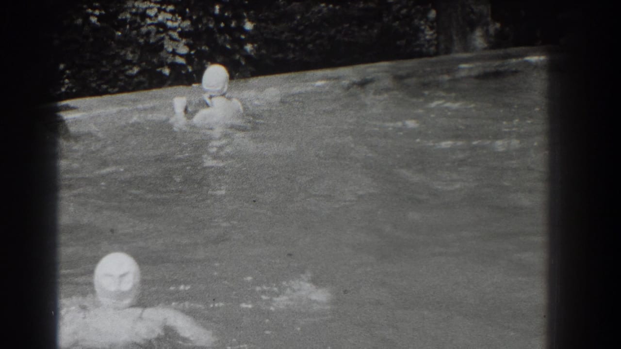 Two capped swimmers in a pool, one closer to the camera and one farther back near the edge.