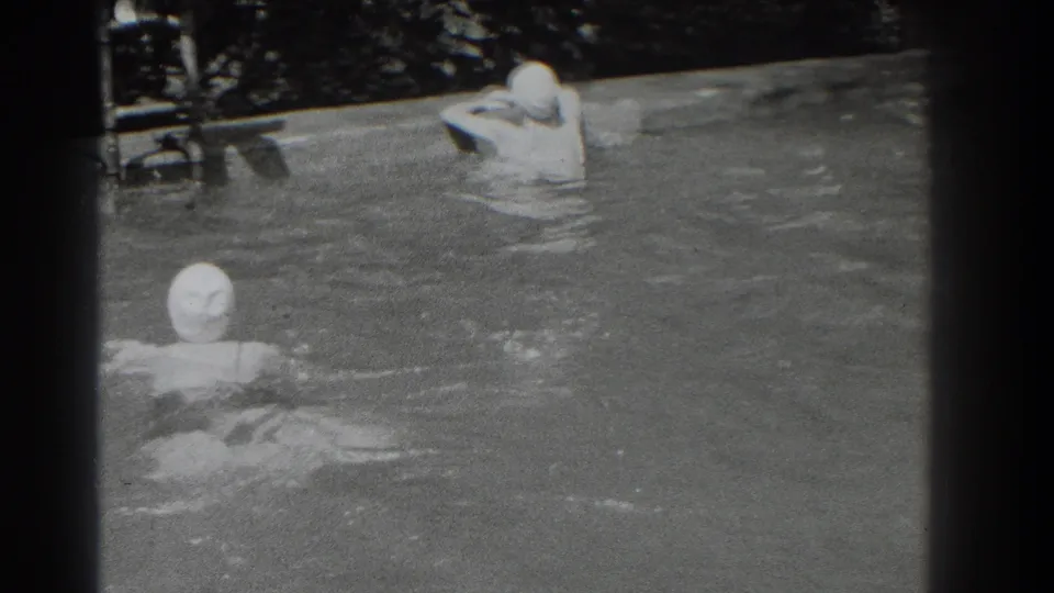1937 Southampton home-movie frame showing two capped swimmers in an outdoor pool, with one raising both arms near the far side.