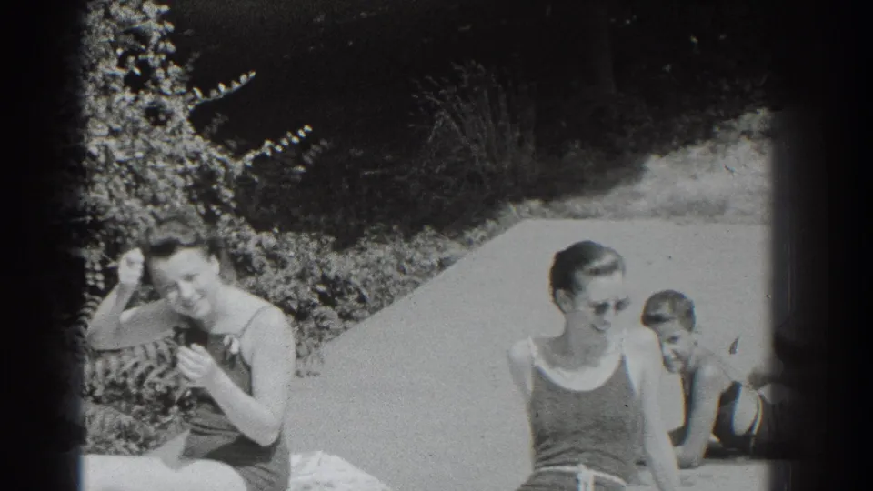 Women in 1930s swimsuits sit by a Southampton pool, with a child nearby and garden planting behind them.