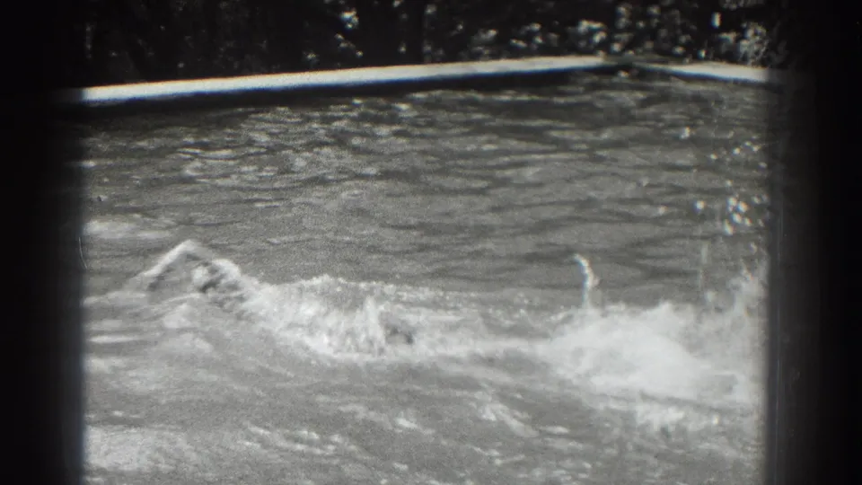 1937 Southampton home-movie frame showing a swimmer partly submerged in a pool, with splashes and ripples across the water.