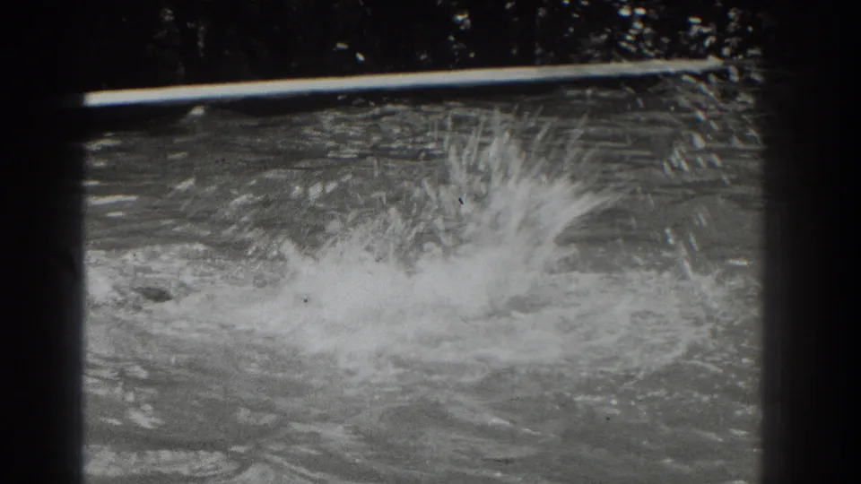 Black-and-white 8mm frame from Southampton showing a swimmer's splash breaking across the pool surface.