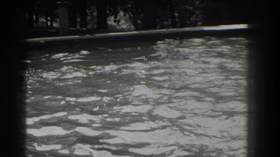 1937 8mm frame of a river surface, with dense ripples, bright water reflections, and a dark wooded shoreline.