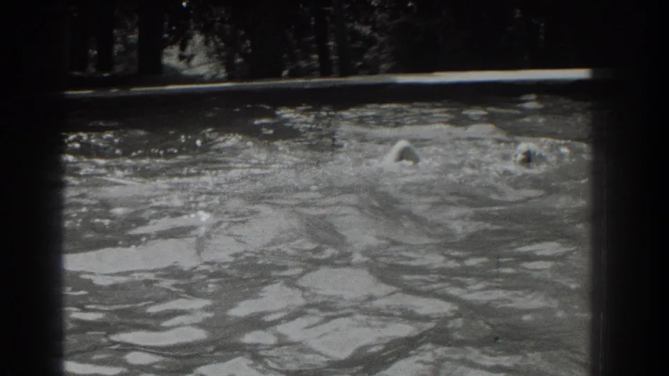 In Southampton, New York, 1937 home-movie footage, a woman in a white swim cap swims across a rippling outdoor pool.