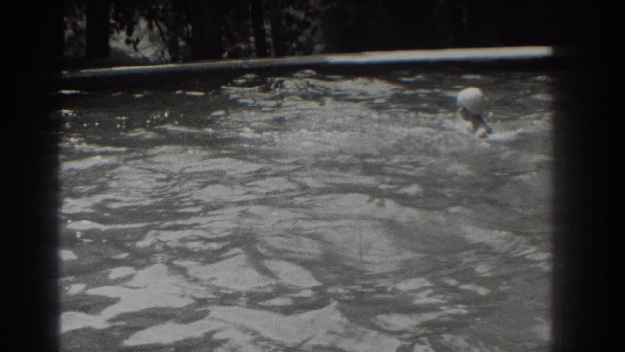 Swimmer in a white cap surfaces near the right side of a rippling outdoor pool.