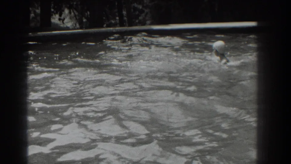 The swimmer surfaces near the right side of the pool, with splashing water and dark trees visible in the 1937 Southampton footage.