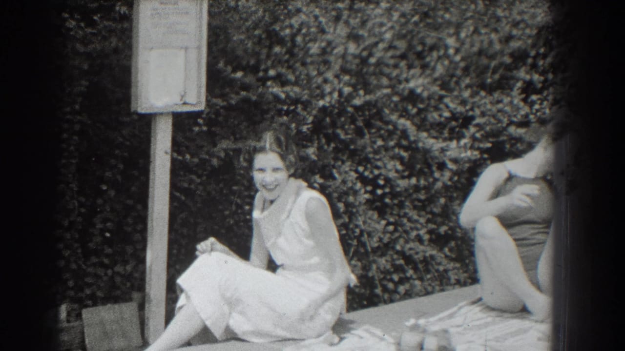 Two women seated by a hedge beside a poolside signpost.
