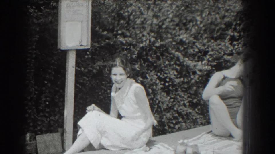 Black-and-white 1937 home-movie frame of two women relaxing on towels near a hedge in Southampton, New York.