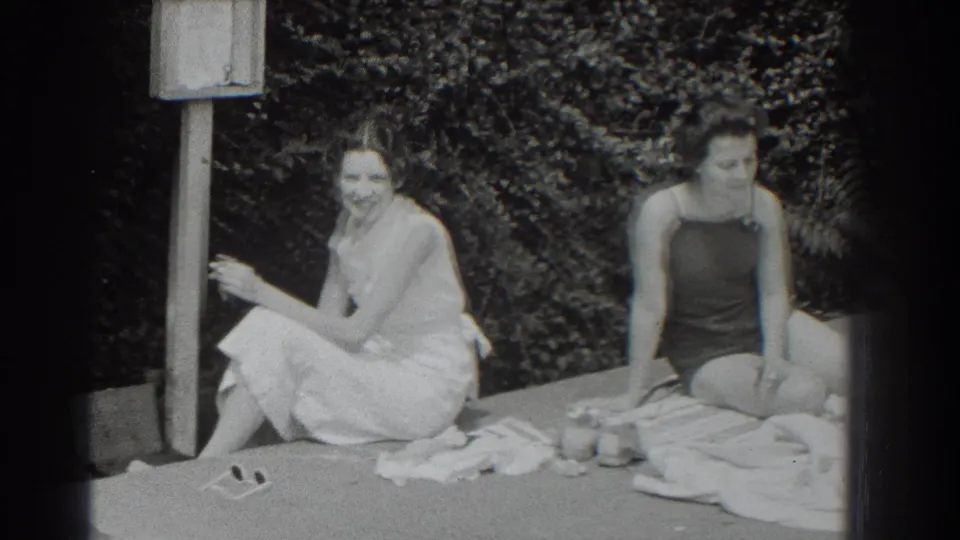 Black-and-white Southampton home-movie frame from 1937 with two women relaxing and smiling at poolside.