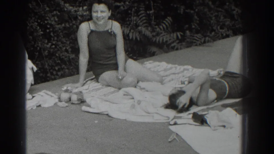 Southampton 1937 home-movie frame of a woman laughing in a dark bathing suit with a reclining companion and towels nearby.
