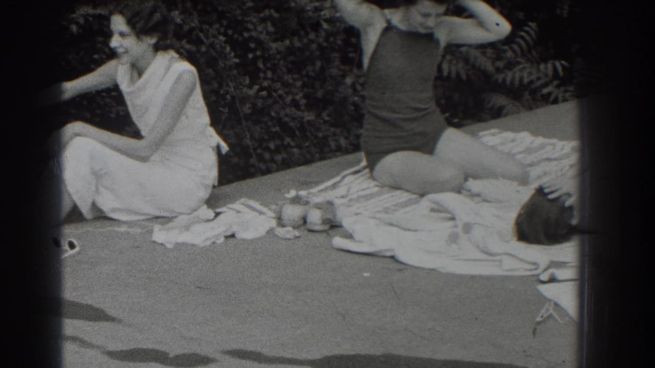 Two women sit outdoors on towels, one in a light dress and one in a dark swimsuit.