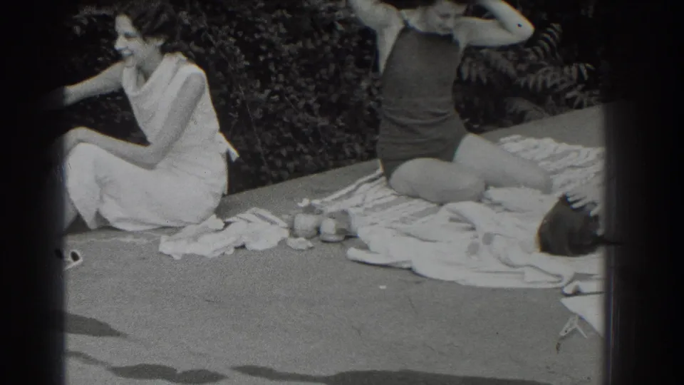 1937 Southampton home-movie frame showing two women relaxing outdoors, with towels and small objects on the ground.