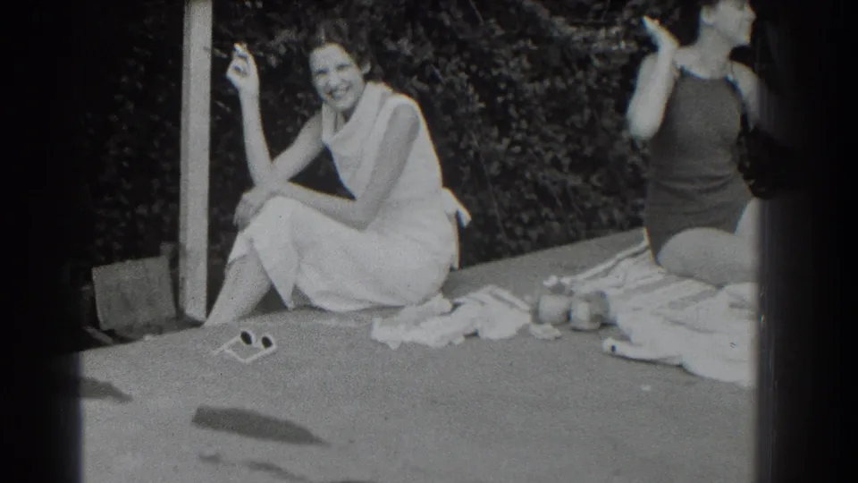 Black-and-white 8mm frame from Southampton showing two women seated outdoors with towels and sunglasses nearby.
