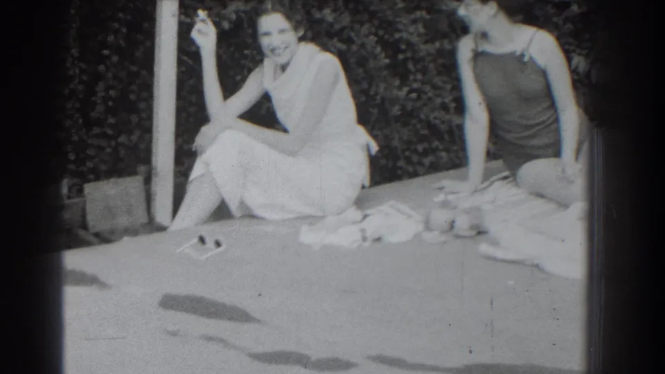 1937 Southampton home-movie frame of two women relaxing outside, one in a light dress holding a cigarette.