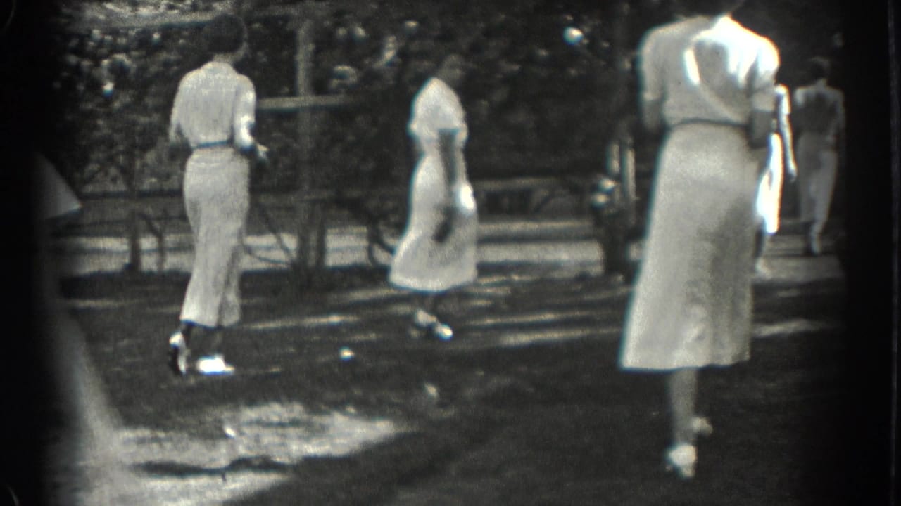 Women in white dresses walk away across a sunny park lawn.