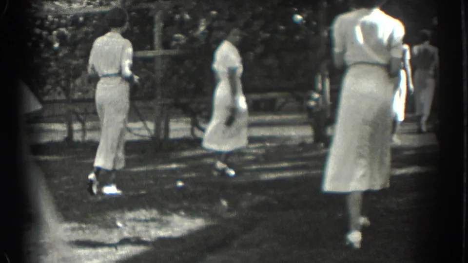 1937 Southampton home-movie frame showing women in white dresses walking through a shaded park area.