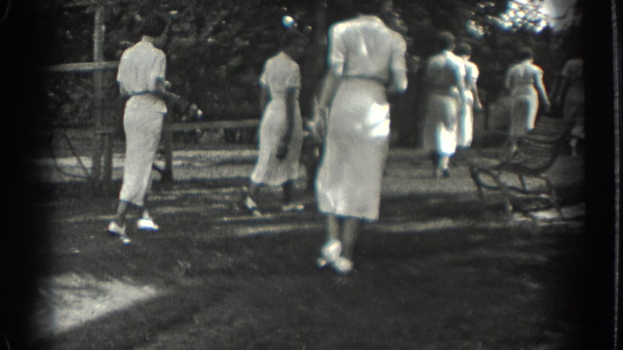 Several women in light dresses walk away through a park.
