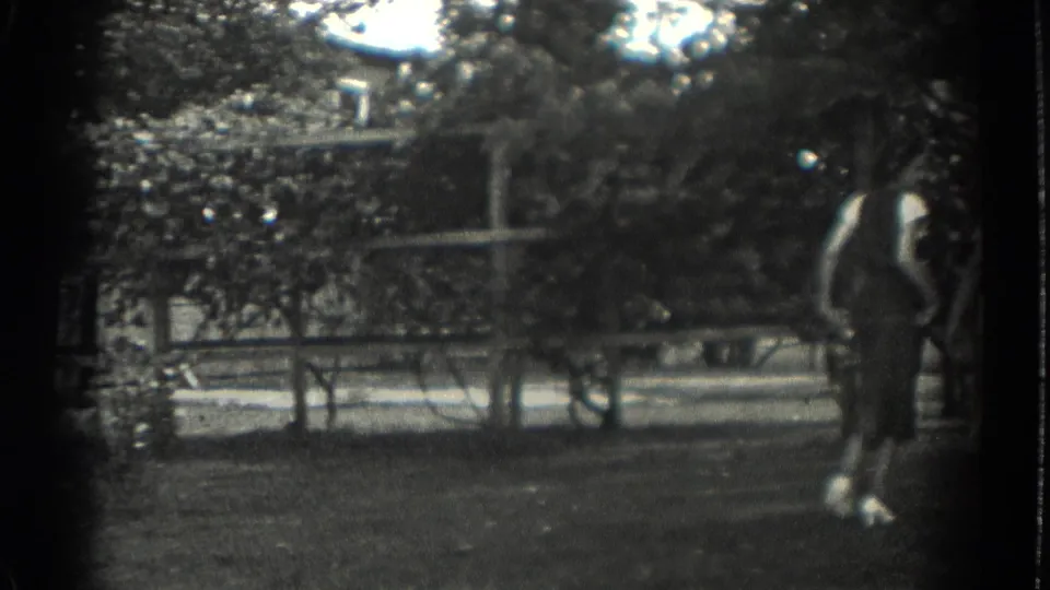 1937 Southampton, New York home-movie frame showing a woman near a park bench, with trees and a path beyond.