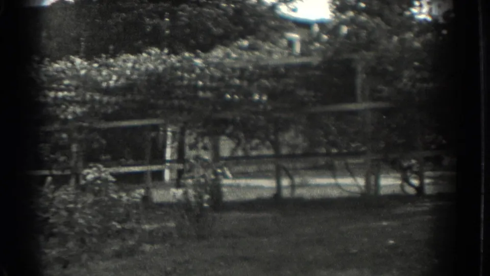 1937 Southampton, New York frame showing a shaded park bench area with trees, foliage, and a path or road beyond.