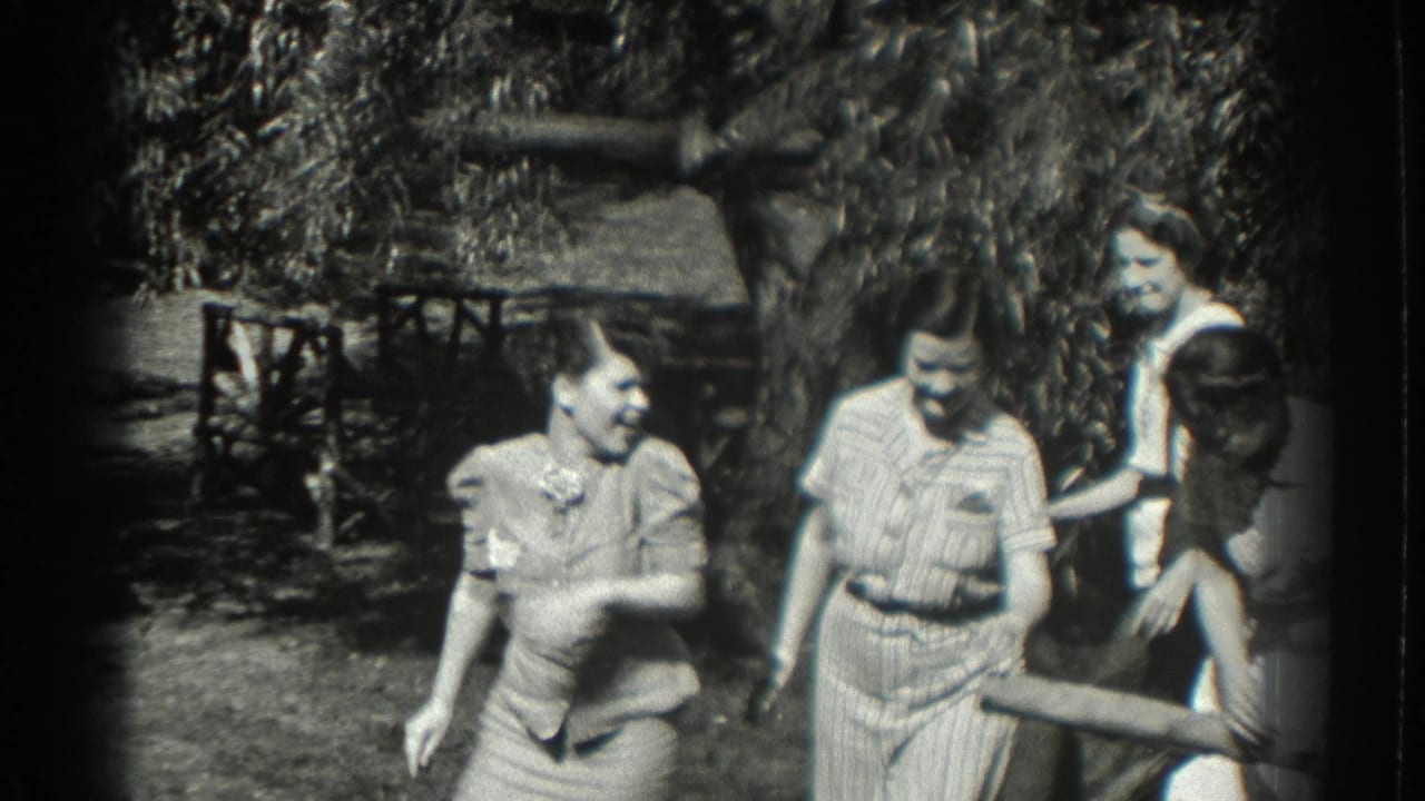 Women in vintage summer clothing smile and talk in a shaded garden.