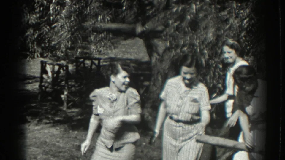 In supplied 1937 Southampton home-movie footage, women in summer dresses and blouses socialize near trees and rustic garden railings.