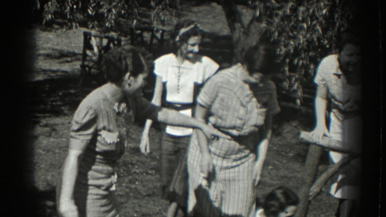 A group in 1930s-style summer clothing stands close together in a Southampton garden, with faces visible and a casual social exchange underway.
