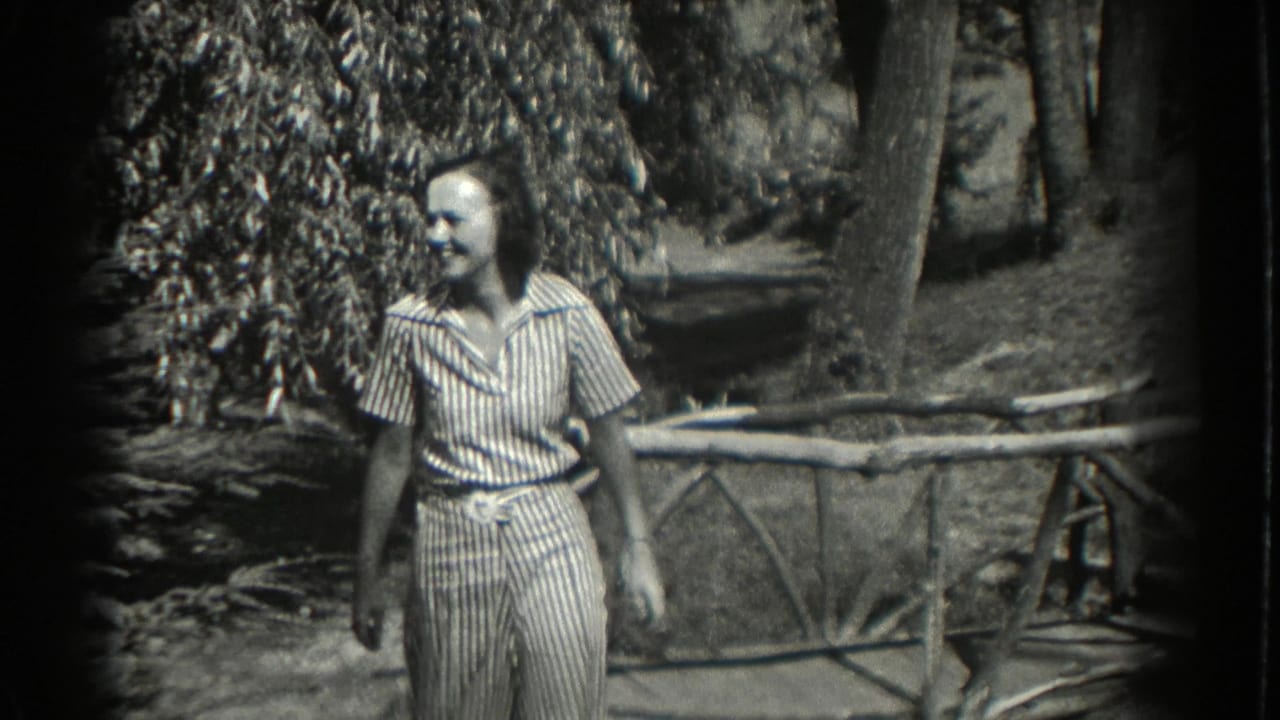 Smiling woman in a striped dress walking beside a rustic fence and trees.